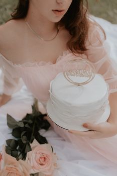 A woman in a pink dress holding an anniversary cake with roses outdoors.
