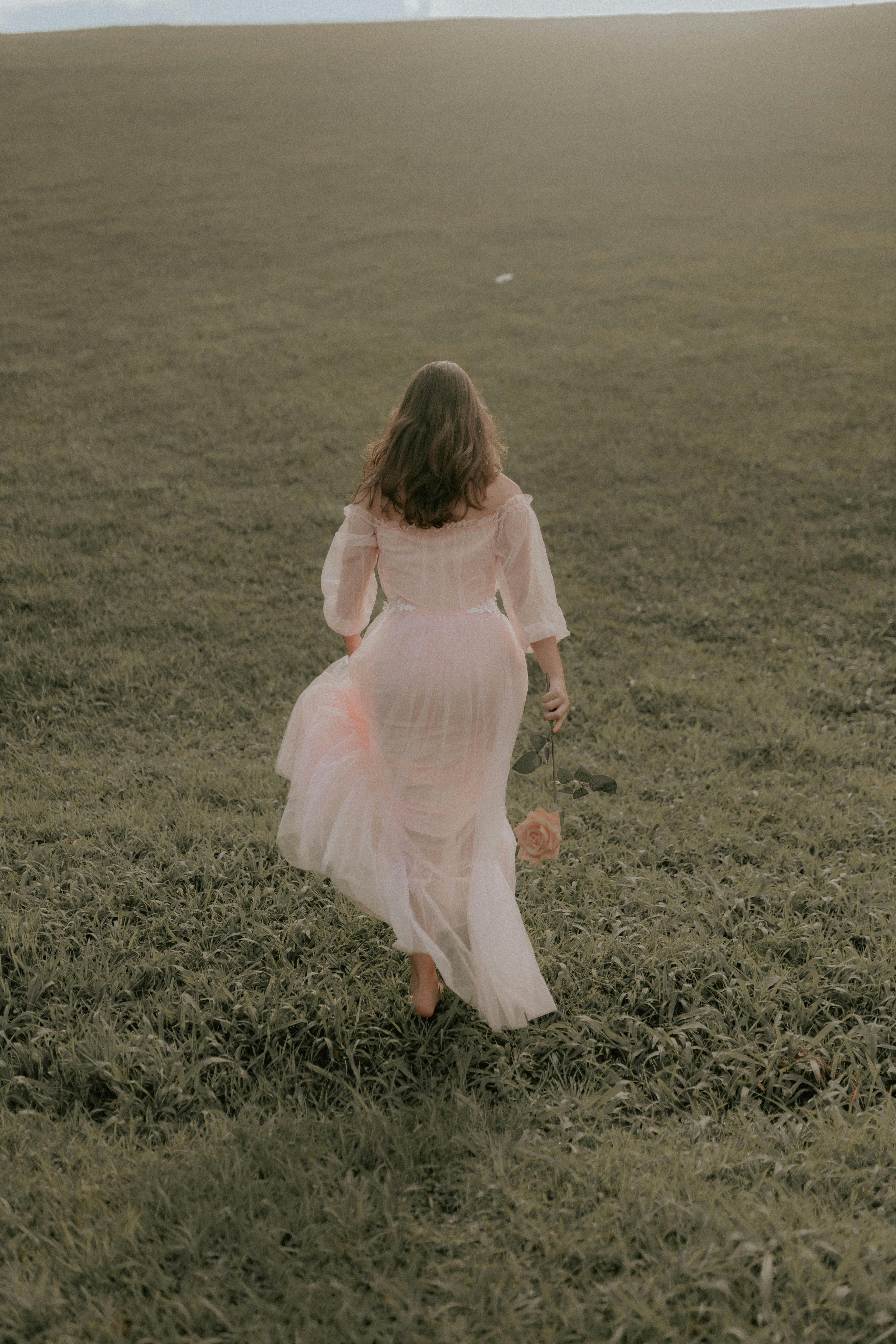 A woman in a flowing white dress walks barefoot through a summer pasture, capturing tranquility and freedom.