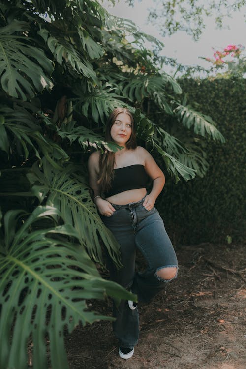 A woman in a crop top and jeans standing in front of a palm tree