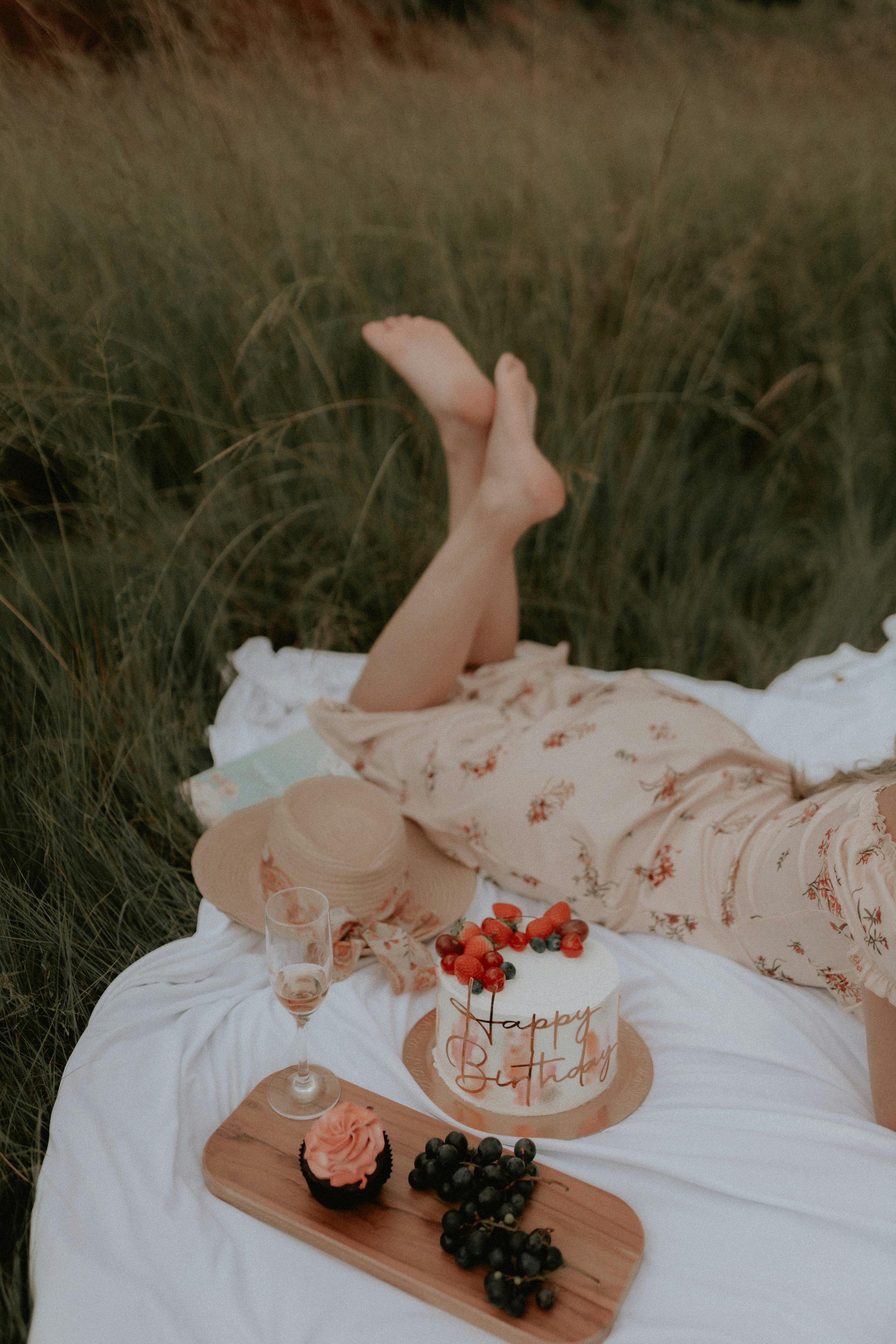 A relaxing summer birthday picnic with cake, cupcake, and grapes set against a lush green meadow.