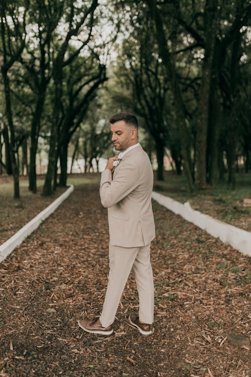 A man in a tan suit stands in the woods
