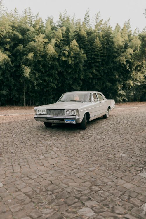 Free Classic Ford Galaxie car parked on a cobblestone road near a lush green forest. Stock Photo