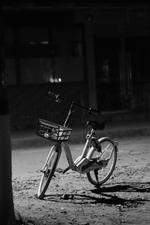 Free Lonely bicycle rests on an urban street at night, captured in monochrome. Stock Photo