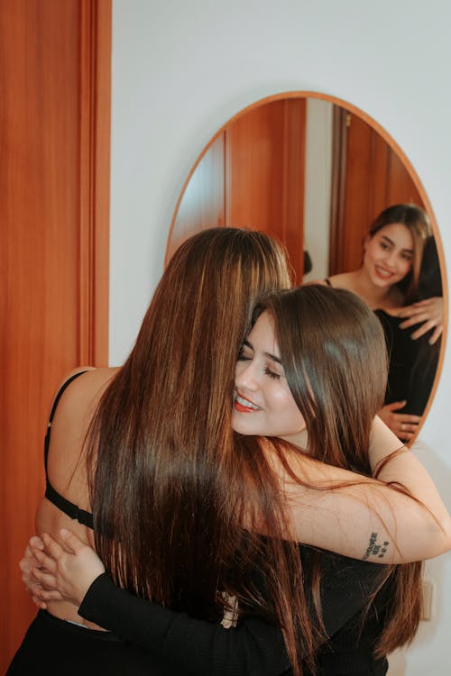 Two women hugging each other in front of a mirror