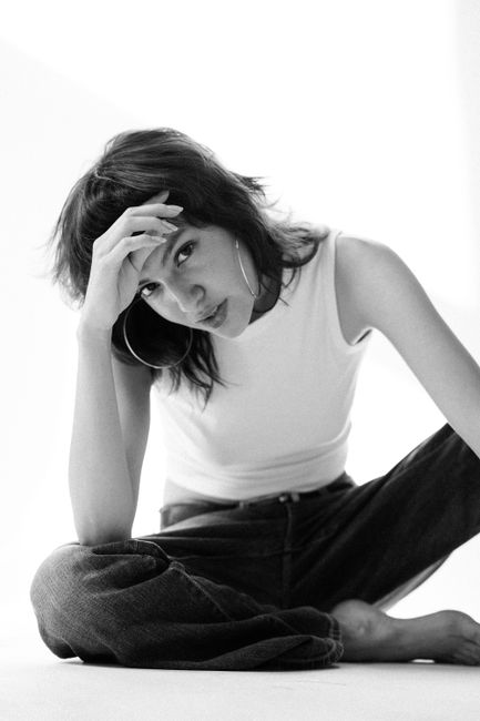 Black and white studio portrait of a woman sitting in casual fashion, exuding style and simplicity.