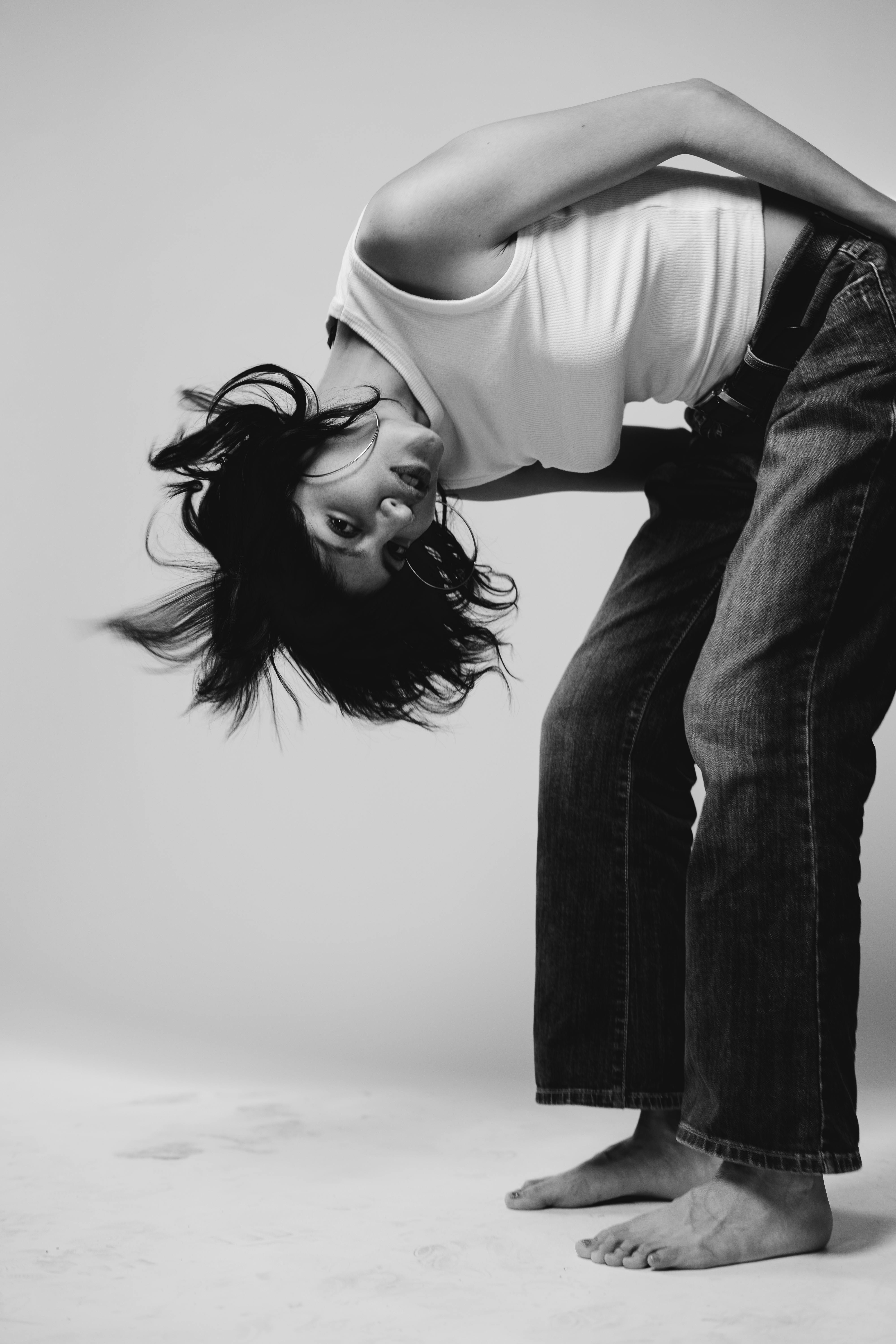 A black and white image capturing a young woman posing creatively in a studio setting.