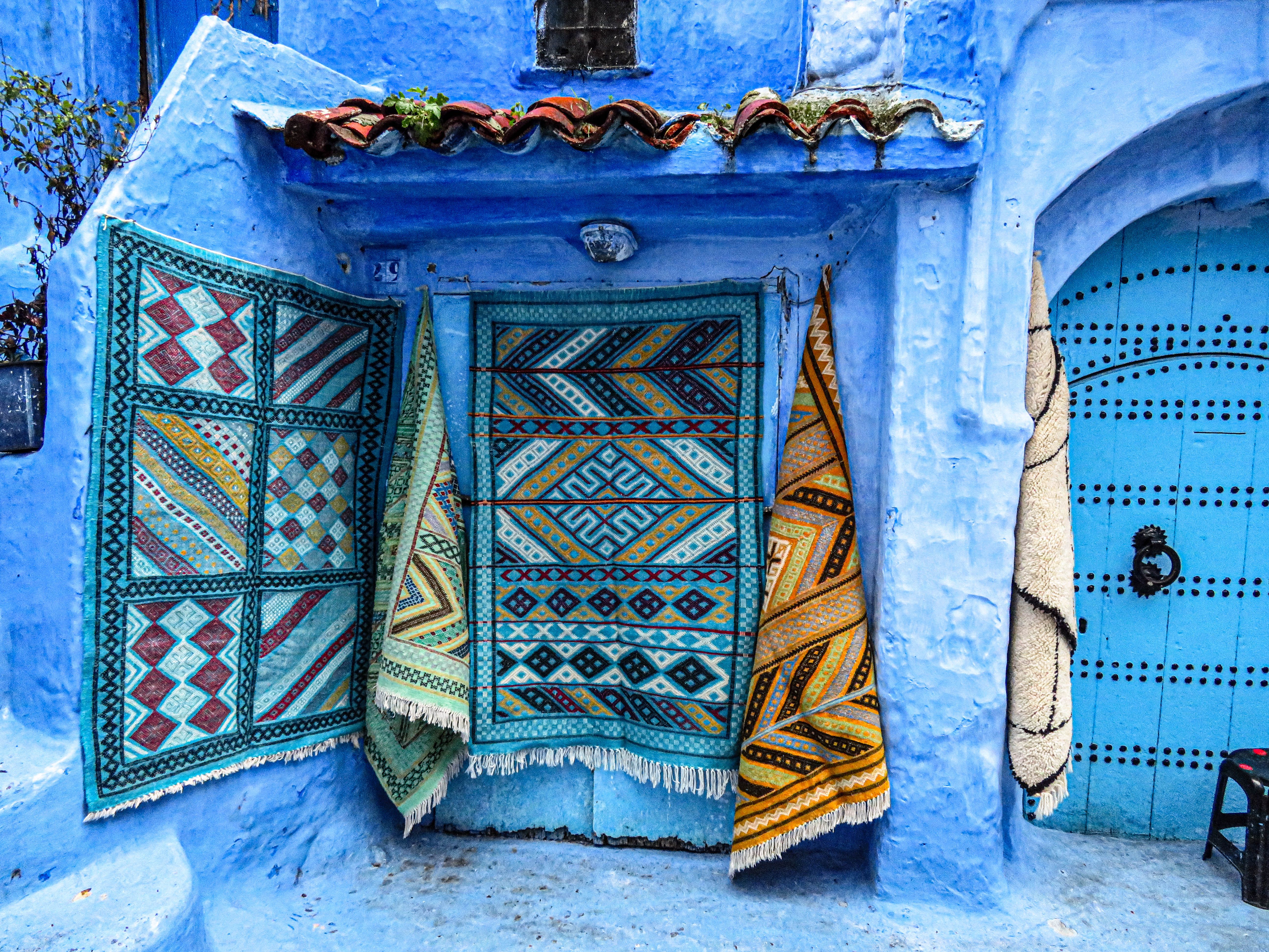 Colorful handmade carpets hang on vibrant blue walls in Chefchaouen, Morocco's blue city.