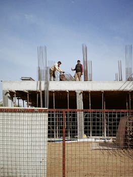 Two workers handling rebar on a construction site under clear blue skies.