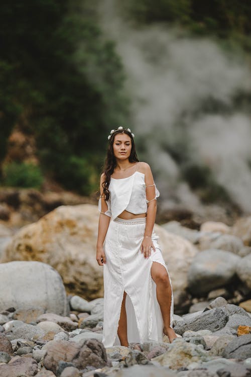 Photo of Woman in White Outfit  and Flower Crown Standing on Rocks