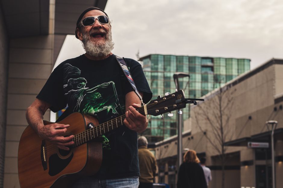 Senior male street musician joyfully playing guitar in an urban setting.