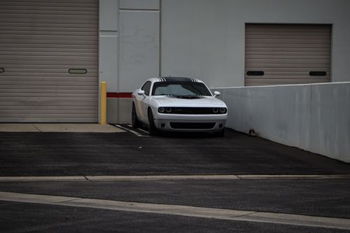 Free A white Dodge Challenger sports car parked in an urban industrial area with rolled-up garage doors. Stock Photo