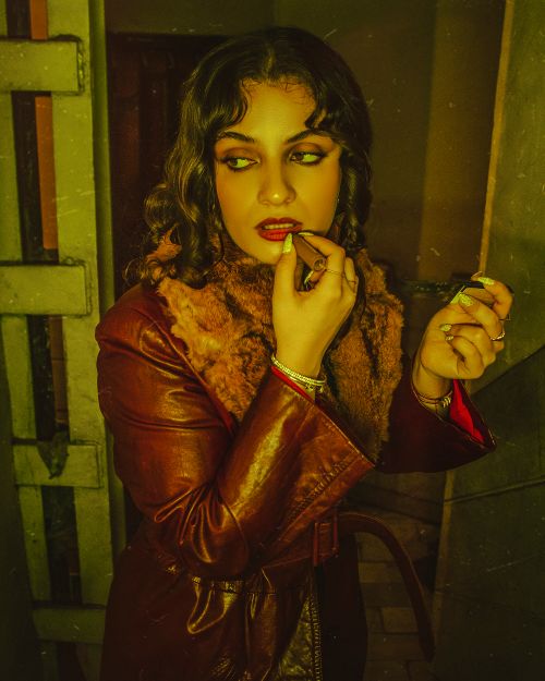 Free Stylish woman in leather coat applying red lipstick in dim light. Stock Photo