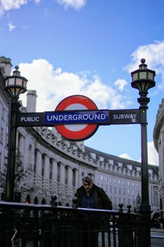 Man at a London Underground entrance with iconic city architecture and clear sky.