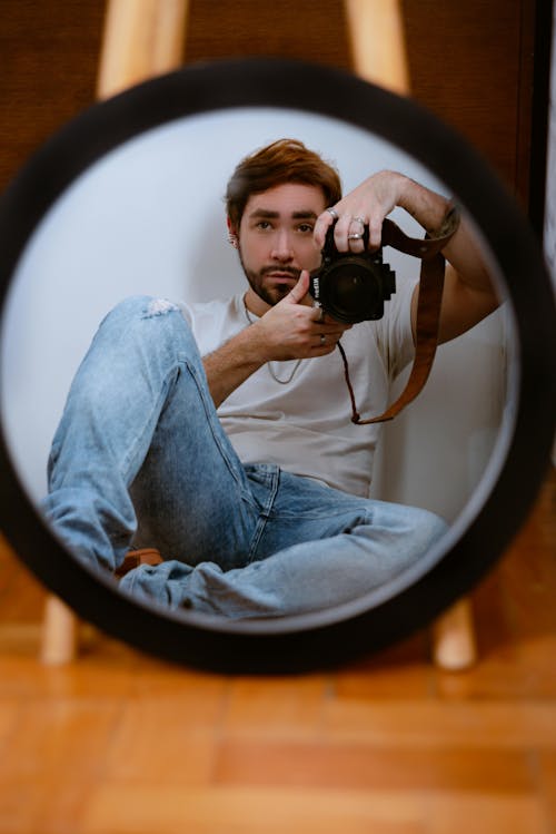 Mirror Reflection of a Man Sitting on a Floor with a Camera in his Hands 