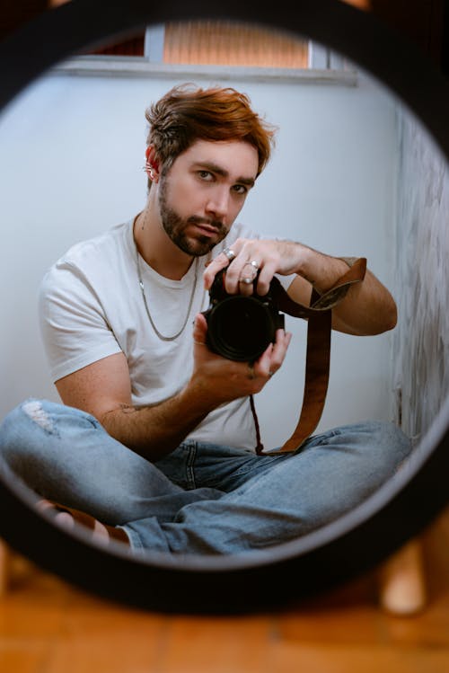 Mirror Reflection of a Man Sitting Crossed-Legged with a Camera in his Hands 