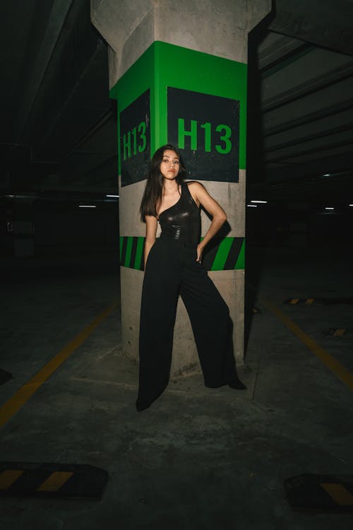A woman in black jumpsuit posing in front of a parking garage