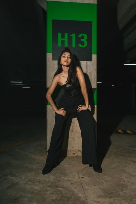 Elegant woman in a sleek black outfit posing confidently in a dimly lit parking garage.