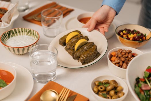 A Mediterranean dining setting with dolmas, salads, and a hand serving food.