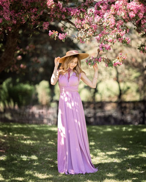 A woman in a long purple dress and hat is standing under a tree