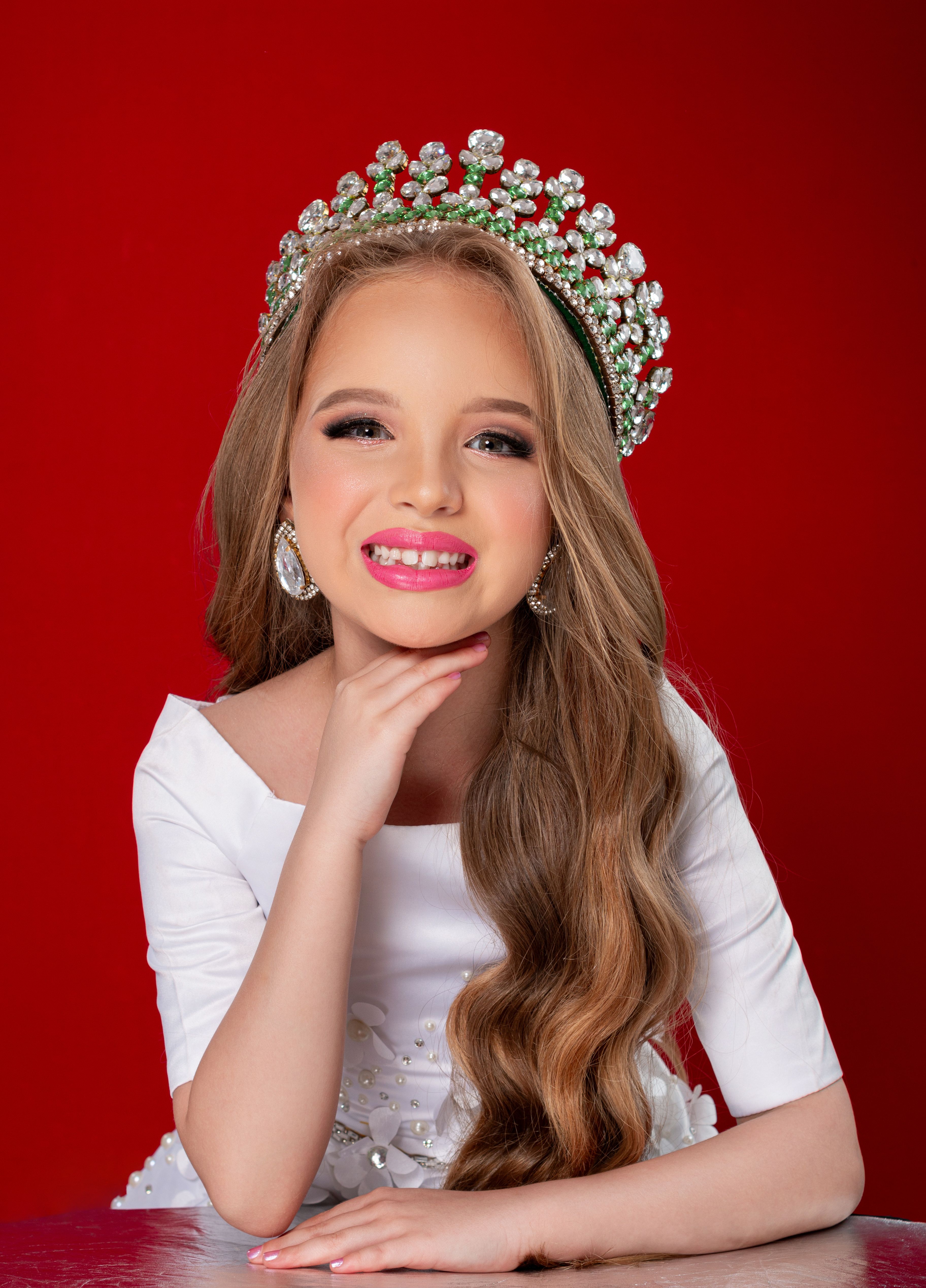 Studio portrait of a smiling girl wearing a crown, set against a vibrant red background.