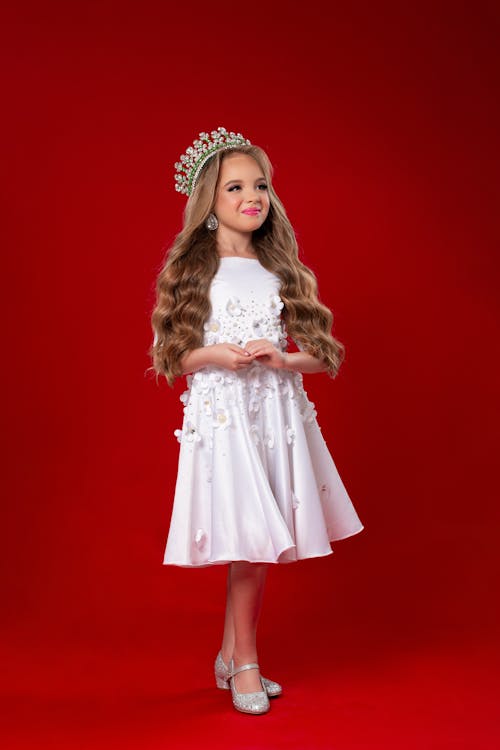 A little girl in a white dress with a crown