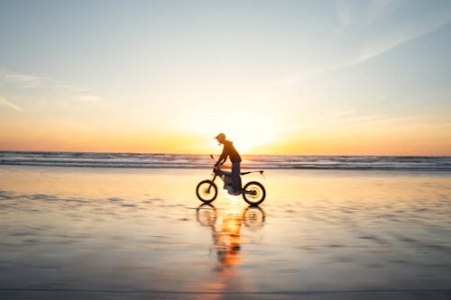 A person riding a bike on the beach at sunset