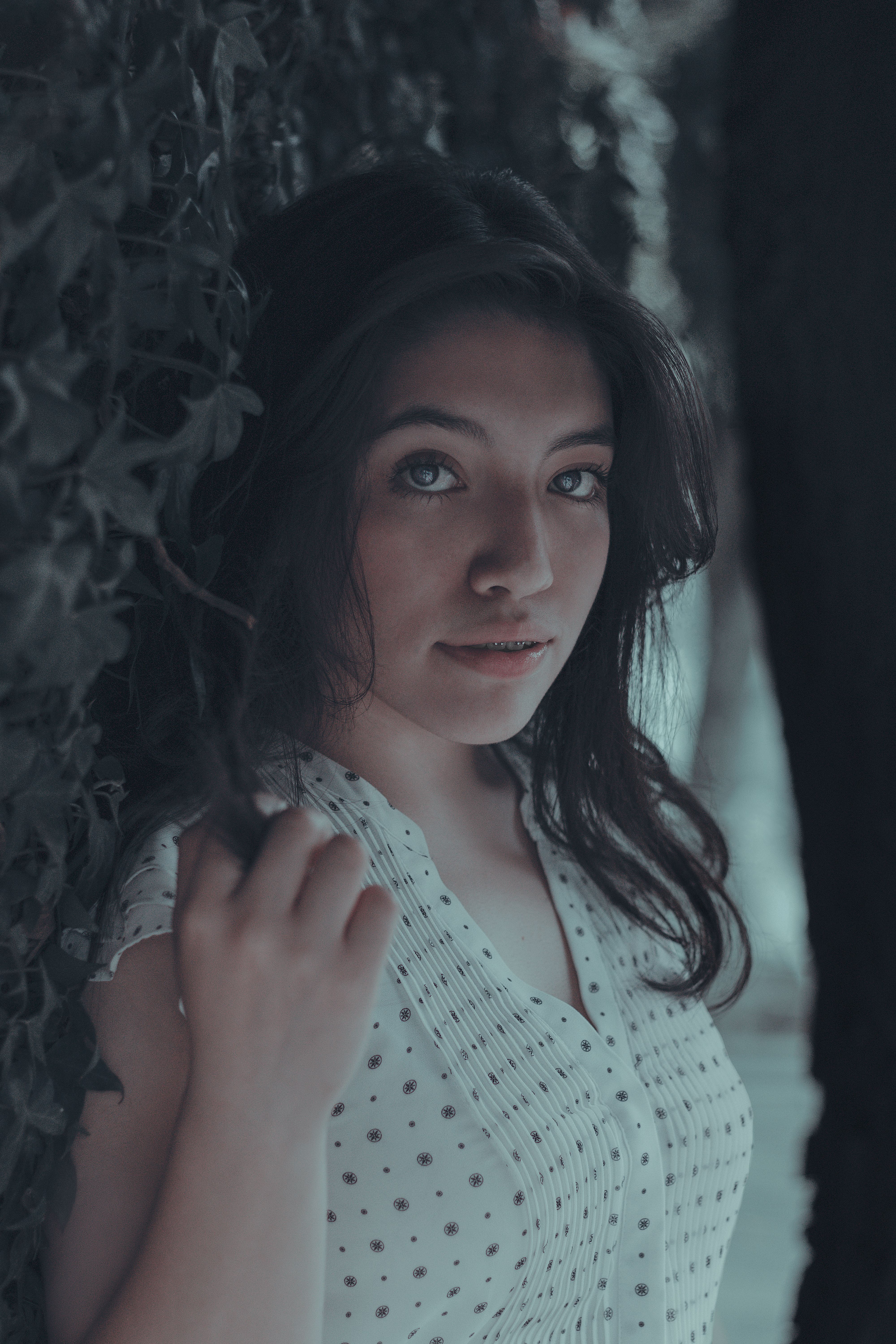 Portrait of a woman with long black hair standing outdoors by leafy vines.