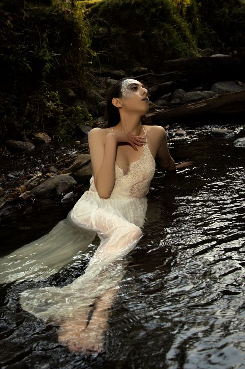 Free Artistic fashion portrait of a woman in a white dress posing in a forest stream, embracing nature's beauty. Stock Photo