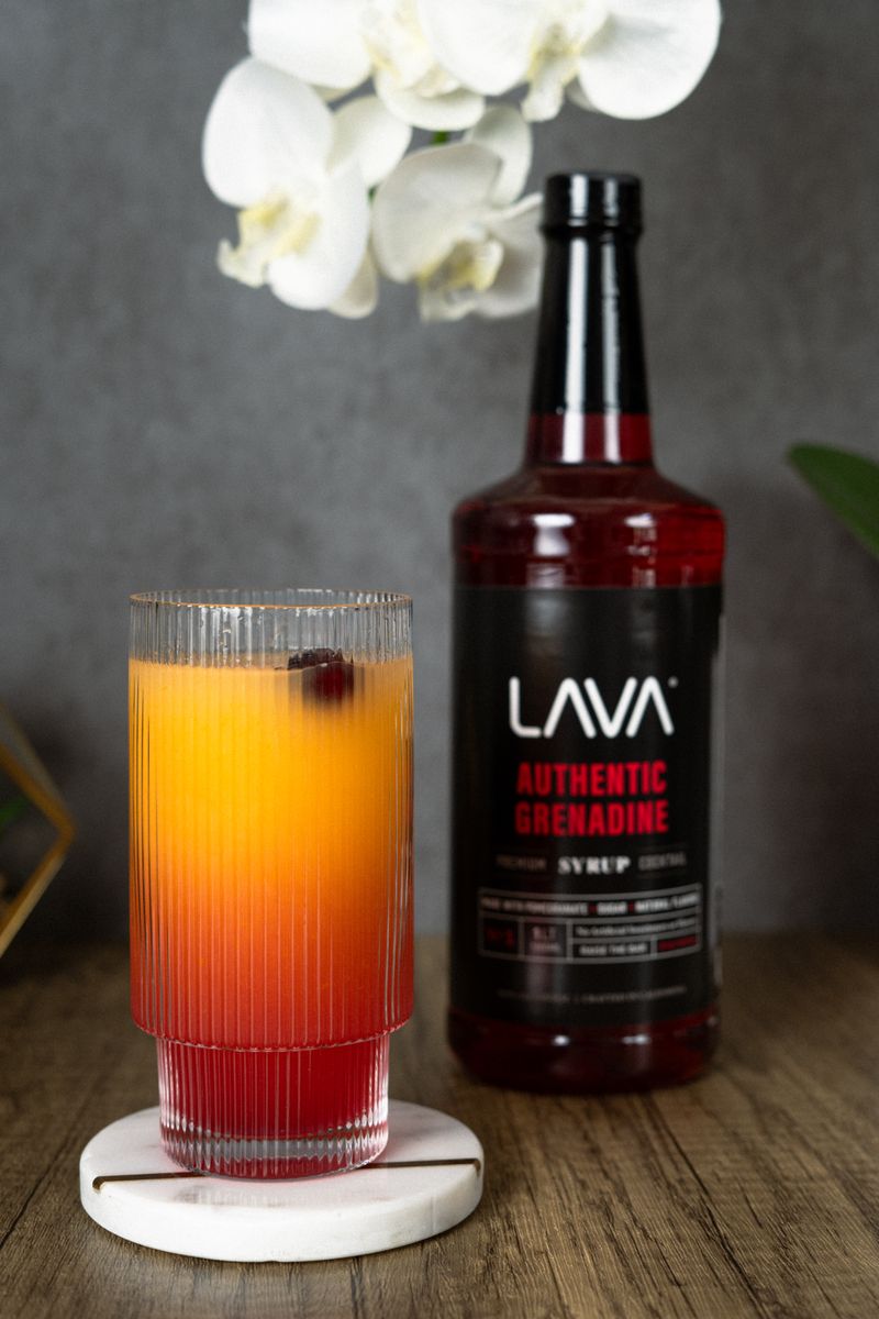 A colorful cocktail with grenadine syrup beside a blooming orchid.
