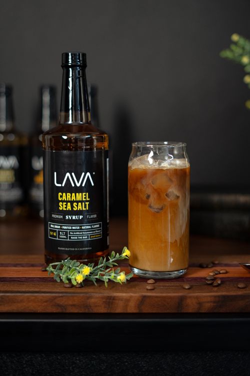 Free LAVA Caramel Sea Salt syrup bottle beside an iced coffee glass on a wooden table. Stock Photo