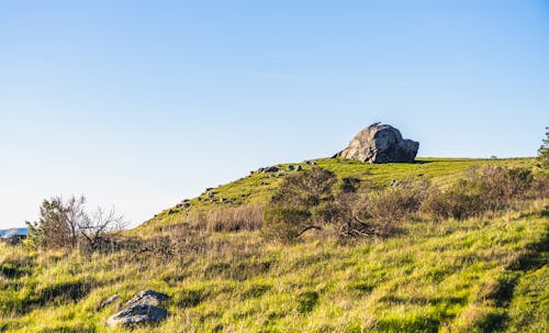 A lone rock sits on top of a grassy hill