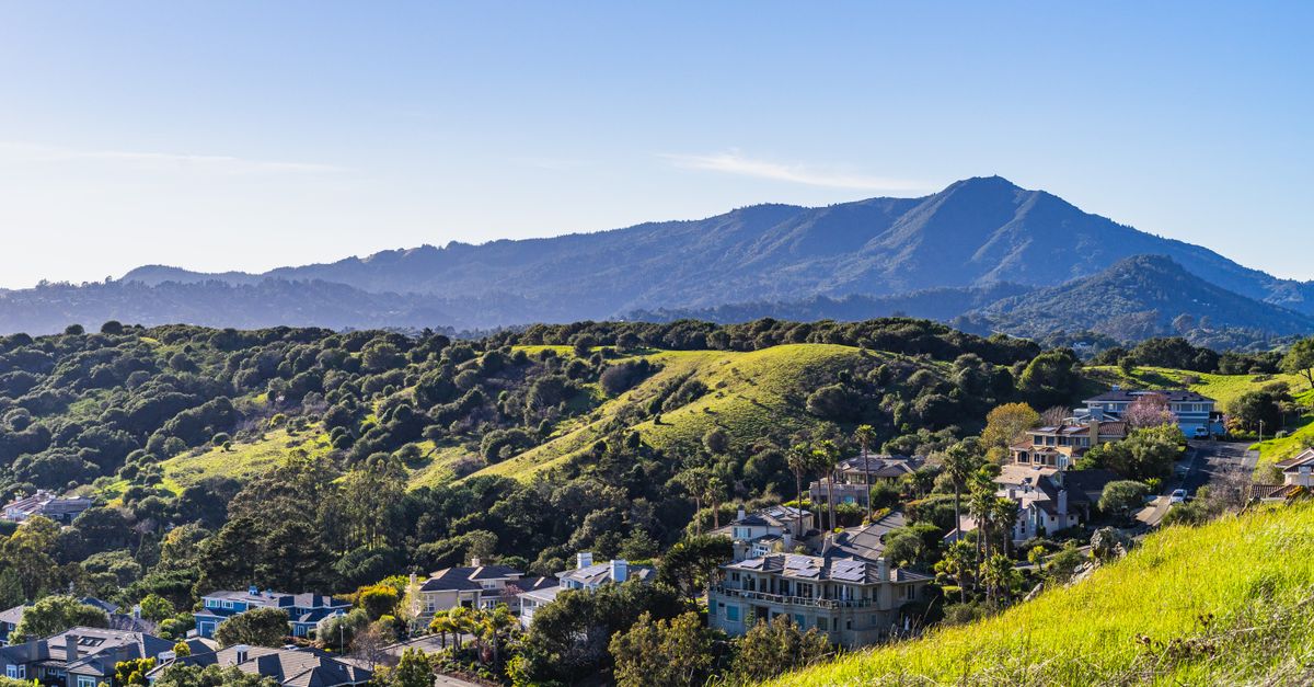 Idyllic townscape surrounded by vibrant green hills with mountain backdrop under clear skies.