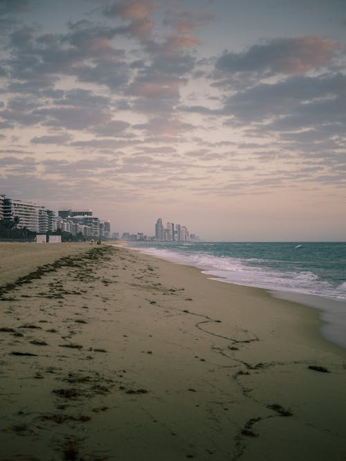 a sandy beach next to the ocean with buildings in the background