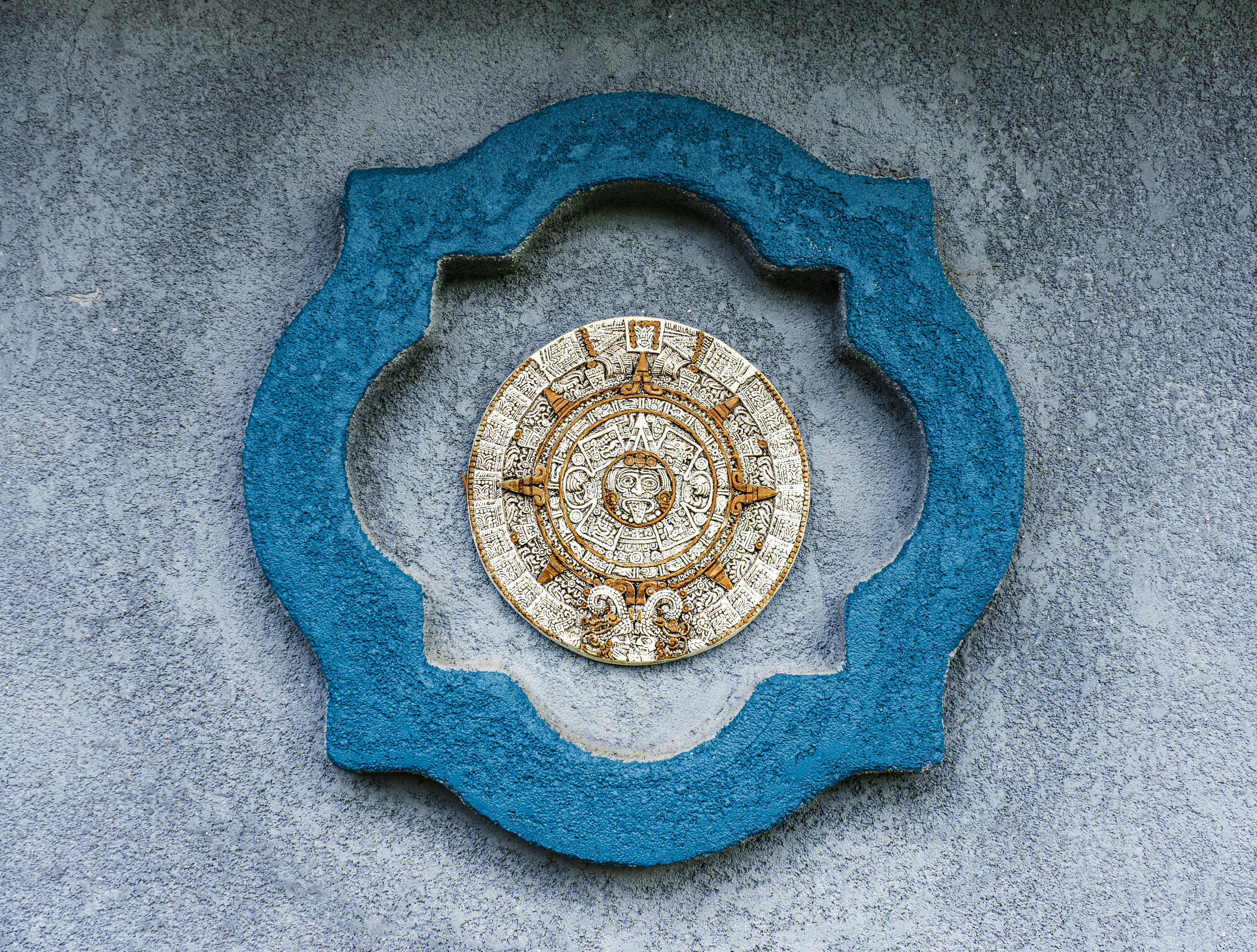 Decorative Aztec calendar on a blue and gray wall, showcasing intricate historical design.
