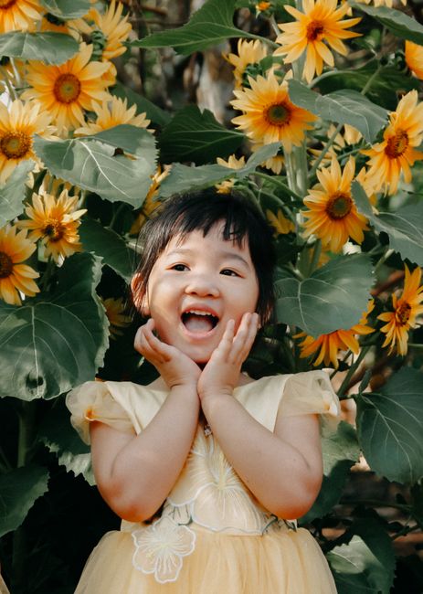 A young girl joyfully smiling amidst vibrant sunflowers on a sunny day.