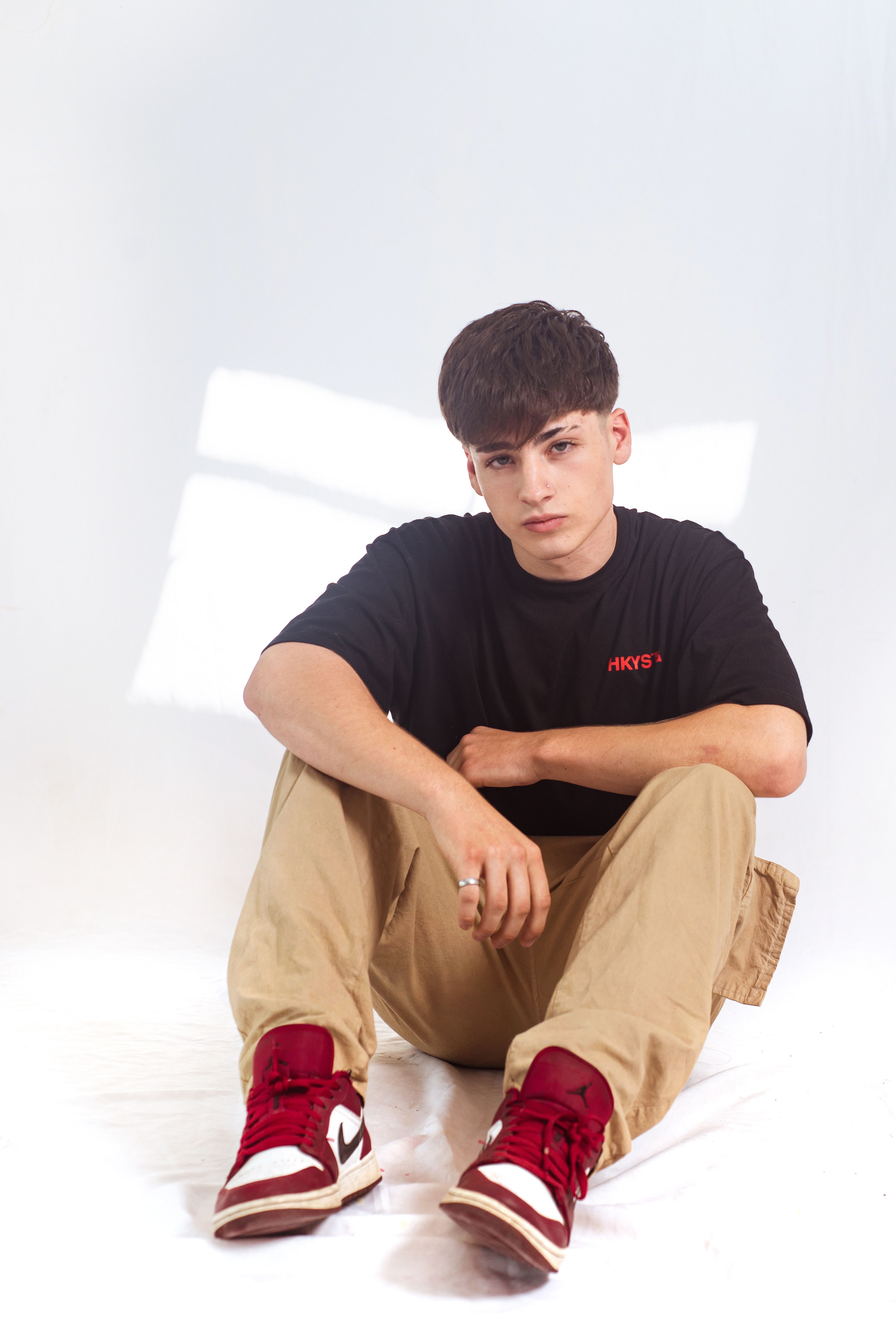 Young male model in urban streetwear sitting in a modern studio setting.