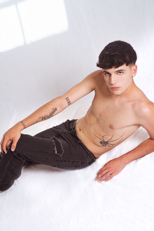 Free Young man sitting topless with tattoos on a white background in a studio setting. Stock Photo