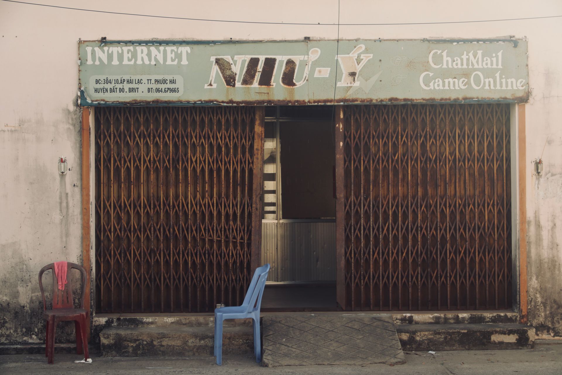 Rustic facade of an internet cafe in Vietnam, featuring wooden gate and empty chairs.