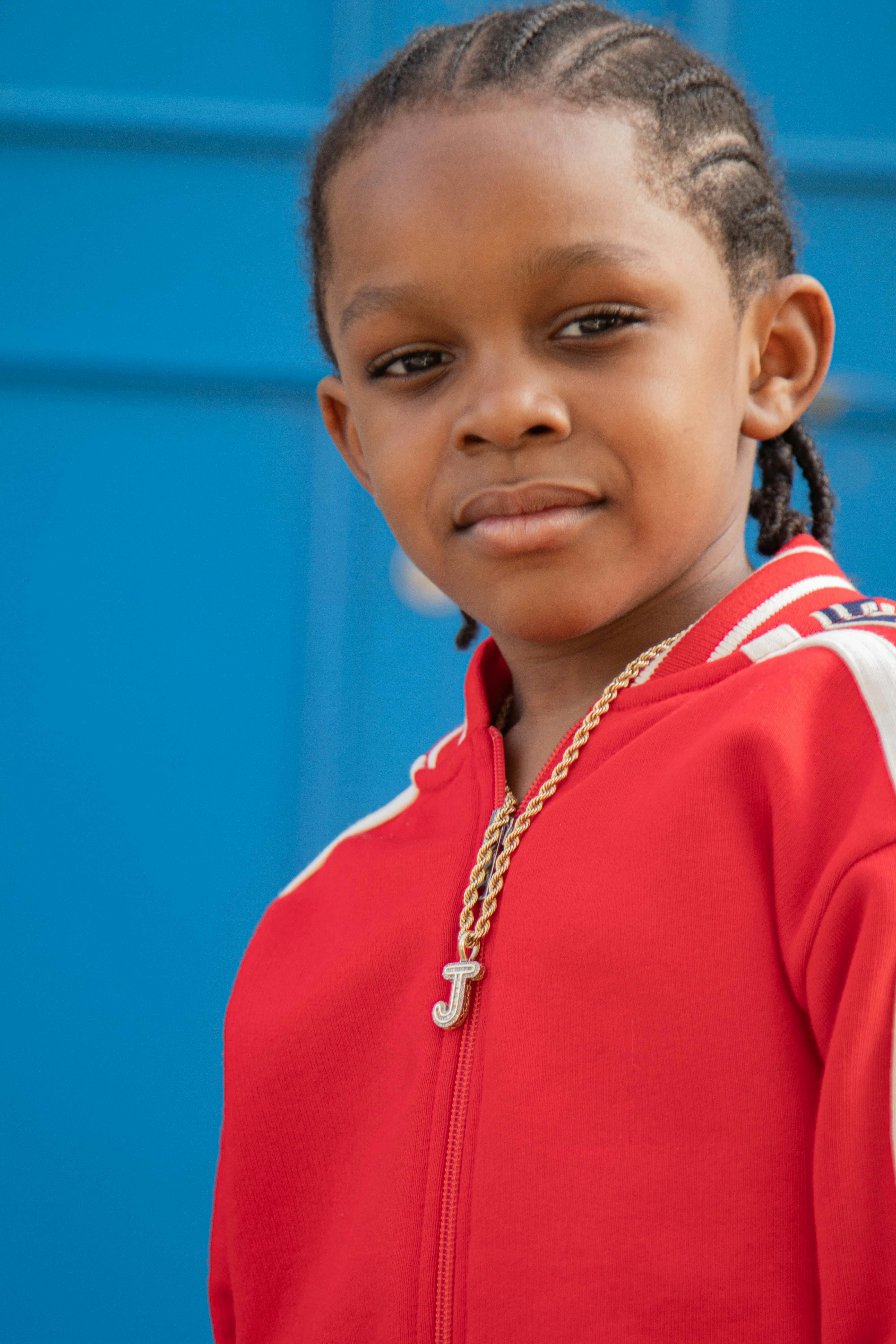 Portrait of a young African boy with braided hair wearing a red sweatshirt and gold chain.