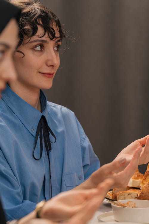 A woman in a blue shirt is sitting at a table with food