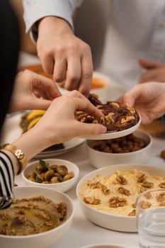 Hands reaching for Mediterranean dishes during a communal meal setting, highlighting community and food sharing.