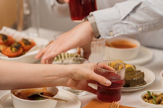 Hands exchanging glasses of refreshing juice at a diverse meal setting.