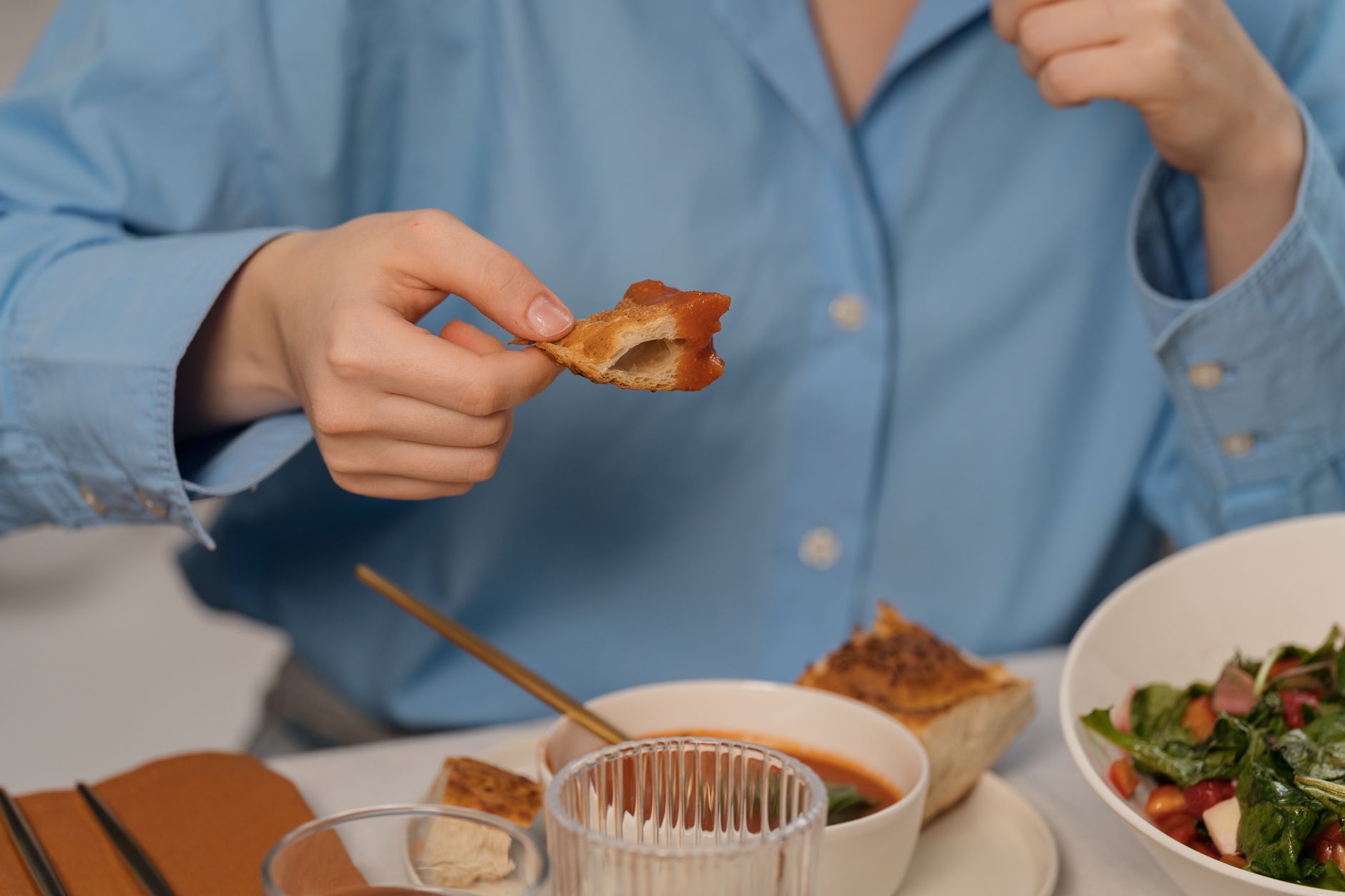 Close-up of a person enjoying bread with soup and salad, showcasing a casual dining setting.
