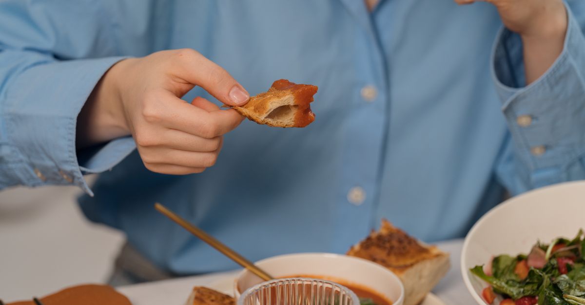 Close-up de uma pessoa desfrutando de pão com sopa e salada, mostrando um ambiente de jantar casual.