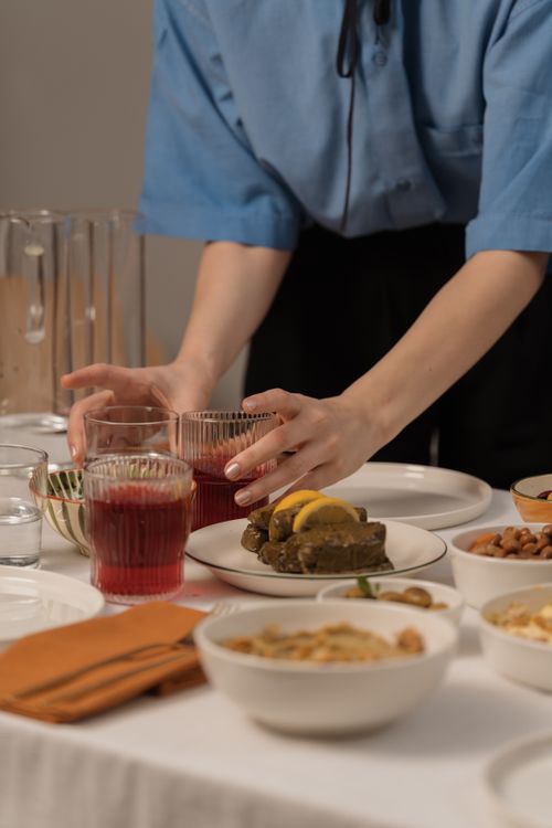 Free Woman in blue shirt arranging drinks on a set table with appetizers. Stock Photo