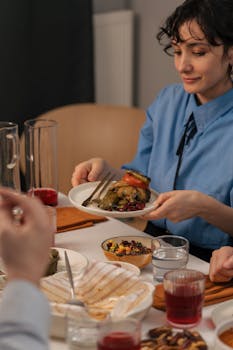 Woman in a blue shirt serving a delicious Mediterranean meal at a cozy dining table.