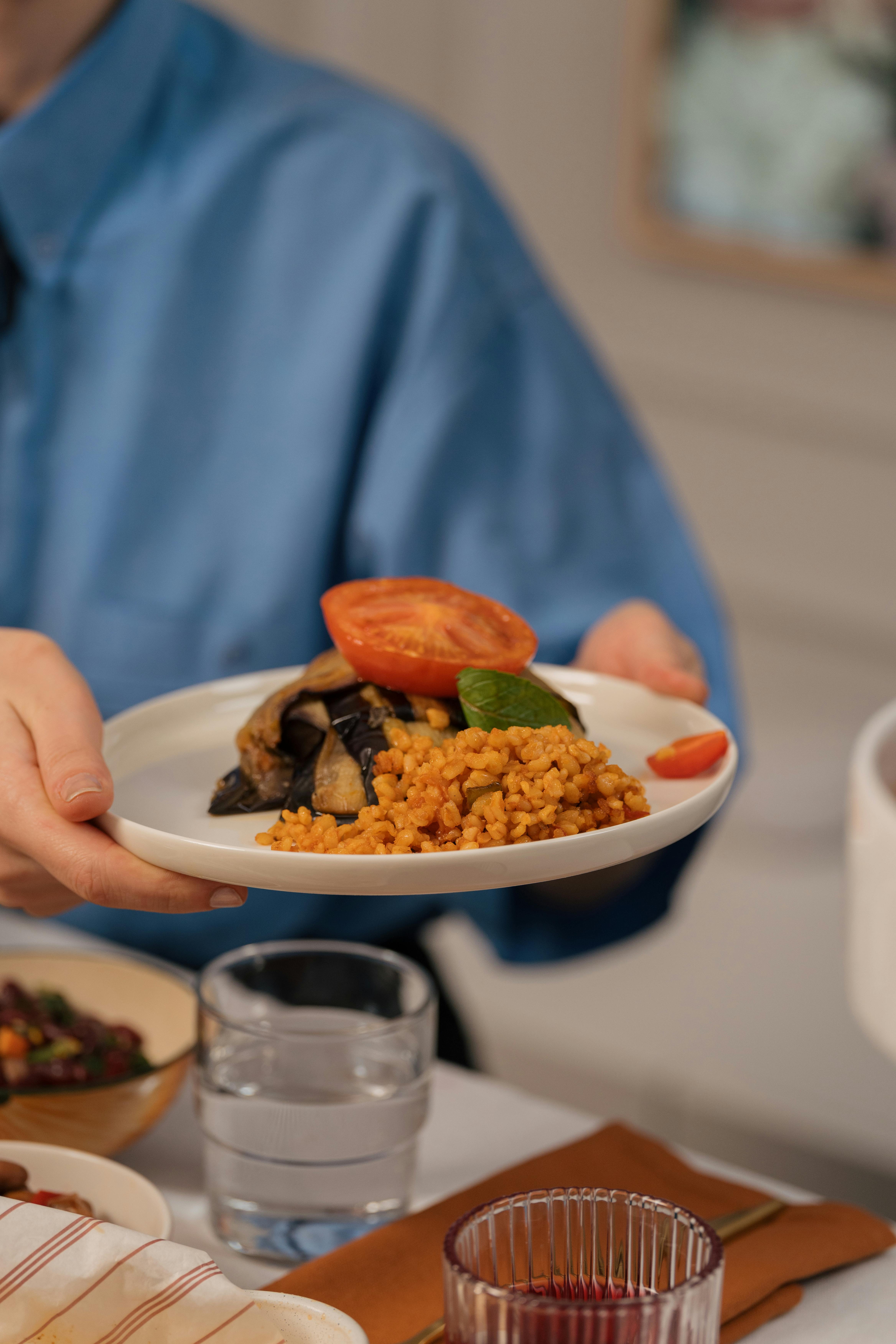 Person presenting a dish with couscous, eggplant, and tomato for a Mediterranean meal.