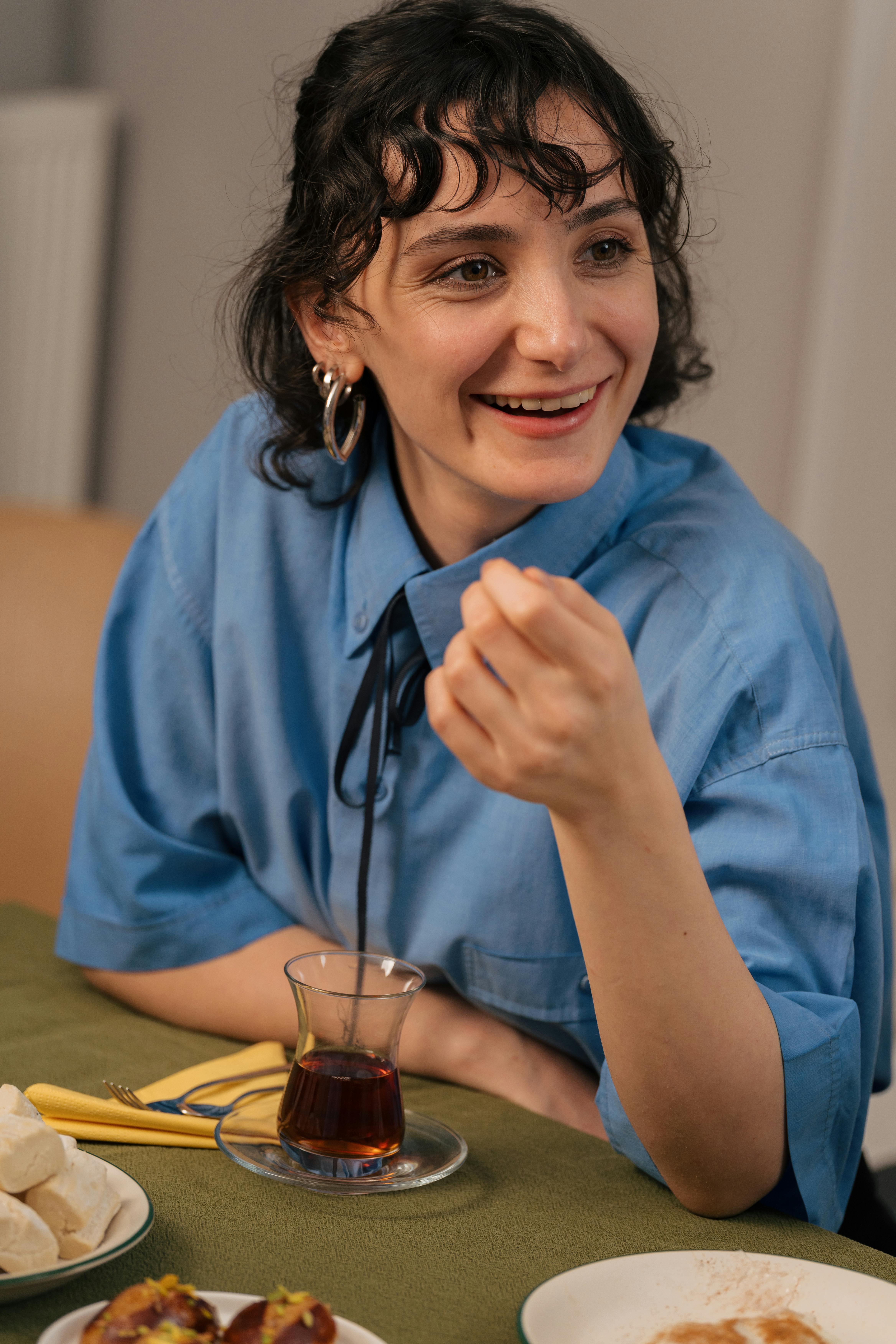 Cheerful woman in blue blouse enjoying a social gathering with tea.