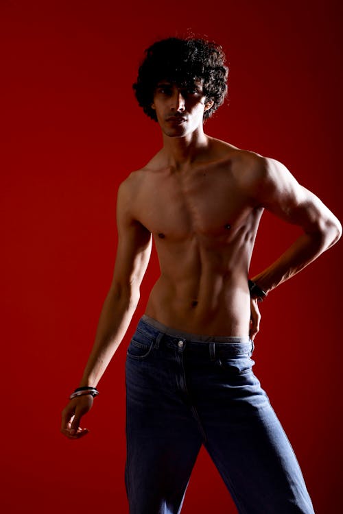 A shirtless man posing in jeans and a red background