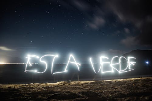 A person writing in the sand with the word esta vee